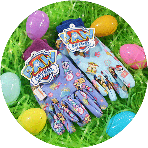 A pair of purple and a pair of light blue Paw Patrol branded kids garden gloves, laying on green easter grass with colorful eggs around it.